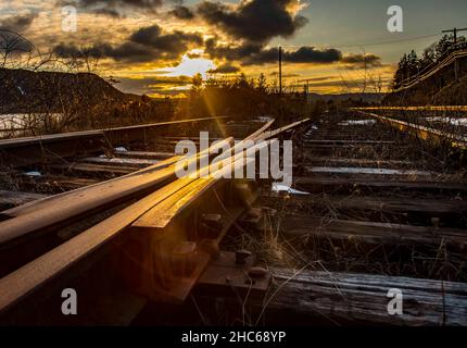 Low-Angle-Aufnahme von Schienen während des Sonnenaufgangs unter dem wolkigen Himmel Stockfoto