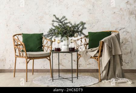 Tannenzweige mit Weihnachtskugeln in Vase, Tassen Tee auf Tisch und Stühlen in der Nähe der hellen Wand Stockfoto