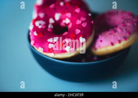 In einer blauen Schüssel gibt es leckere süße rosa Donuts mit Streuseln in Form von Herzen. Ein niedliches Geschenk zum Valentinstag. Backwaren. Stockfoto