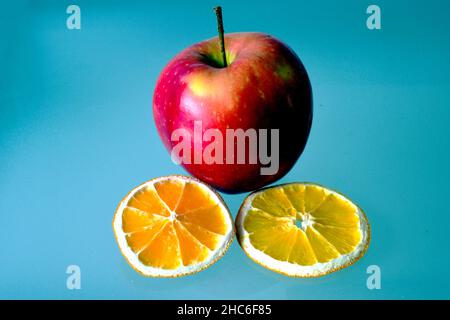 Isolierter roter Apfel und dekorative trockene Orangenfrucht-Scheiben auf glänzender Glasoberfläche.e glänzende Reflexion. Makroansicht. Gesunde Ernährung. Vegetarischer Lebensstil. Stockfoto