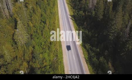 Fliegen Sie über die schönen Waldbäume und die Straße. Luftaufnahme. Auto auf einer kurvenreichen Straße in den Hügeln. Luftkamera aufgenommen. Panorama im Landschaftsformat. Luftaufnahme Stockfoto