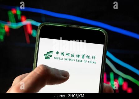 China. 09th Dez 2021. In dieser Abbildung ist das Logo der chinesischen Handelsbank Postal Savings Bank of China (PSBC) auf einem Smartphone mit einem Index-Diagramm der wirtschaftlichen Börse im Hintergrund zu sehen. (Foto von Budrul Chukrut/SOPA Images/Sipa USA) Quelle: SIPA USA/Alamy Live News Stockfoto