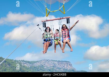 Drei Mädchen genießen es mit einem Fallschirm über dem Meer. Unterhaltungskonzept Stockfoto