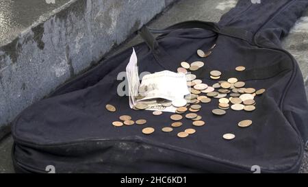 Russische Rubel fallen auf schwarzem Gitarrenkoffer auf dem Bürgersteig der Stadt im Freien. Nahaufnahme für Papiergeld und Münzen, die auf schwarzem, leerem Gitarrenkoffer liegen, Armut CO Stockfoto
