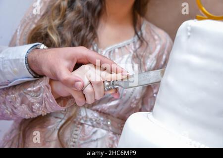 Braut und Bräutigam schneiden die Hochzeitstorte . Bräutigam ist in blauen Hochzeitsanzug und Braut in einem weißen Hochzeitskleid gekleidet. Stockfoto
