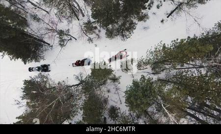 Die Luftaufnahme eines Teams von oben hielt an, als es mit Schneemobilen in den Winterwäldern unterwegs war. Die Sportler auf Schneemobilen bereit, durch tiefen Schneesturf zu bewegen Stockfoto