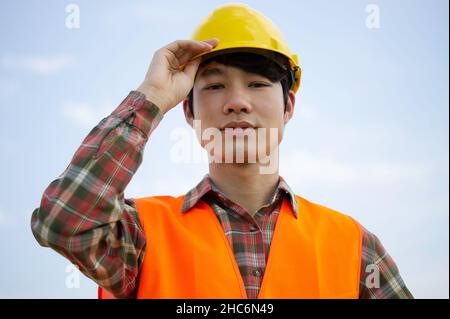 Nahaufnahme eines jungen asiatischen Ingenieurs in reflektierendem Look. Das Hemd und der Ständer halten den Helm in einem Happy.and Copy Space. Stockfoto