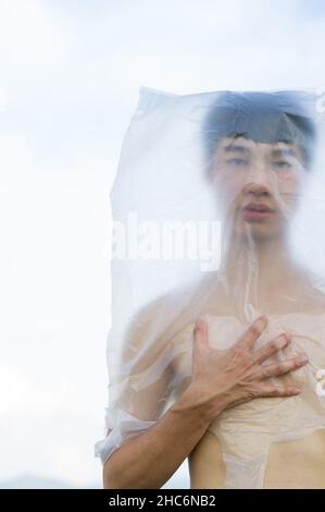 Der schwule Mann aus Asien trägt eine Plastiktüte auf seinem Kopf, die ein Konzept erstickt hat, mit Plastik und Umweltverschmutzung aufzuhören oder Marine und zu stoppen Stockfoto