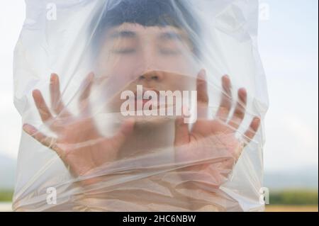 Der schwule Mann aus Asien trägt eine Plastiktüte auf seinem Kopf, die ein Konzept erstickt hat, mit Plastik und Umweltverschmutzung aufzuhören oder Marine und zu stoppen Stockfoto