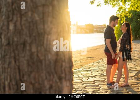 Gemischtrassig junges Paar, das sich mit einem Sonnenuntergang in einem romantischen Sommertermin am Fluss anschaut Stockfoto