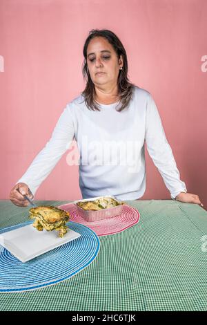 Vertikale Abbildung einer erwachsenen Frau, die eine Portion frisch zubereiteter Pesto-Lasagne auf einem Teller serviert. Stockfoto