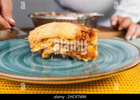 Nahaufnahme einer Hand einer Frau, die eine Portion frisch zubereiteter Lasagne mit Bolognese serviert. Stockfoto