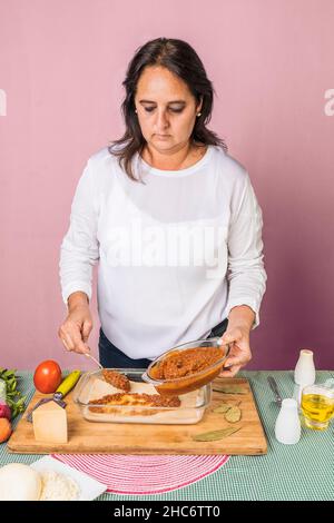 Vertikales Bild einer erwachsenen Frau, die ein Lasagne-Rezept macht, indem sie Bolognese-Sauce auf die Zubereitung setzt. Stockfoto