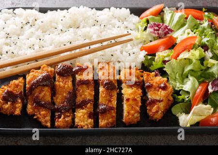 Tori Katsu ein beliebtes japanisches Komfortgericht aus panierten Hähnchenschnitzel, serviert mit Reis- und Gemüsesalat auf dem Betontisch. Horizontal Stockfoto