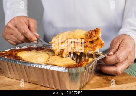 Nahaufnahme einer erwachsenen Frau, die eine Portion frisch zubereiteter Lasagne mit Bolognese zum Essen herausnimmt. Stockfoto