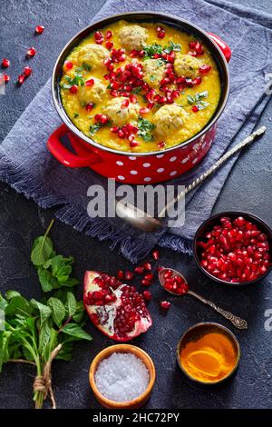 Ash-e Anar, iranische gelbe, geteilte Erbse Granatapfelsuppe mit Lamm Fleischbällchen in einem roten Topf auf einem Betontisch mit vertikaler Ansicht der Zutaten von oben Stockfoto