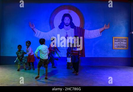 Haulia, Indien. 25th Dez 2021. Kinder kommen aus verschiedenen fernen Dörfern, um Heilige Weihnachten in einer kleinen und einzigen Kirche in der Gegend zu feiern und während der Bedrohung durch Omicron (Covid-19) in Indien in Haulia, Westbengalen, vor einem großen Jesus Christus-Foto ohne Maske zu spielen. (Foto von Soumyabrata Roy/Pacific Press) Quelle: Pacific Press Media Production Corp./Alamy Live News Stockfoto