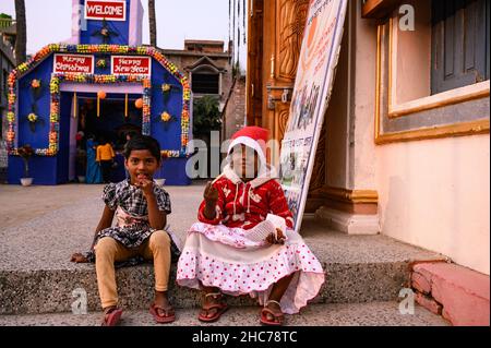 Haulia, Westbengalen, Indien. 25th Dez 2021. Kinder kommen aus verschiedenen fernen Dörfern, um Heilige Weihnachten in einer kleinen und einzigen Kirche in der Gegend zu feiern und während der Bedrohung durch Omicron (Covid-19) in Indien in Haulia, Westbengalen, vor einem großen Jesus Christus-Foto ohne Maske zu spielen. (Bild: © Soumyabrata Roy/Pacific Press via ZUMA Press Wire) Bild: ZUMA Press, Inc./Alamy Live News Stockfoto