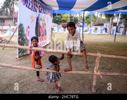 Haulia, Westbengalen, Indien. 25th Dez 2021. Kinder kommen aus verschiedenen fernen Dörfern, um Heilige Weihnachten in einer kleinen und einzigen Kirche in der Gegend zu feiern und während der Bedrohung durch Omicron (Covid-19) in Indien in Haulia, Westbengalen, vor einem großen Jesus Christus-Foto ohne Maske zu spielen. (Bild: © Soumyabrata Roy/Pacific Press via ZUMA Press Wire) Bild: ZUMA Press, Inc./Alamy Live News Stockfoto