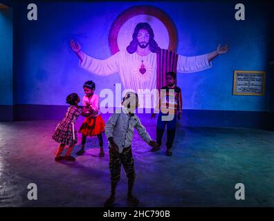 Haulia, Westbengalen, Indien. 25th Dez 2021. Kinder kommen aus verschiedenen fernen Dörfern, um Heilige Weihnachten in einer kleinen und einzigen Kirche in der Gegend zu feiern und während der Bedrohung durch Omicron (Covid-19) in Indien in Haulia, Westbengalen, vor einem großen Jesus Christus-Foto ohne Maske zu spielen. (Bild: © Soumyabrata Roy/Pacific Press via ZUMA Press Wire) Bild: ZUMA Press, Inc./Alamy Live News Stockfoto