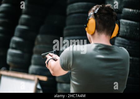 Mann mit orangefarbenen, schalldichten Kopfhörern, der mit einer Pistole schießt Stockfoto