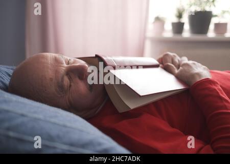 Älterer kaukasischer Mann, der mit einem Buch auf dem Sofa beim Nickerchen schlief Stockfoto