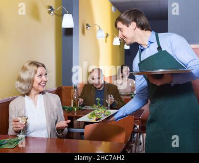 Positiver Kellner, der der reifen Frau Ordnung bringt Stockfoto