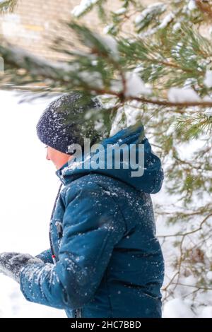 Unschärfe lächelndes Kind Junge im Winterwald im Schneesturm. Lächelndes Kind, das neben dem Baum auf schneebedecktem Hintergrund steht. Aktiv Zeit im Freien verbringen. Kalt her Stockfoto