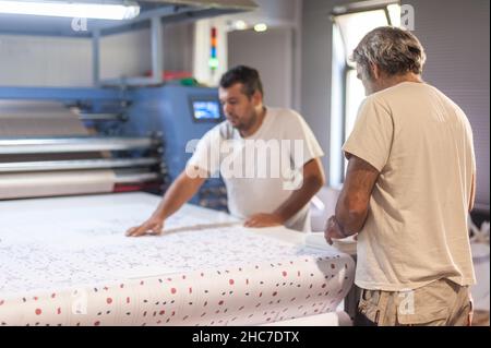 Zwei Techniker Arbeiter Betreiber arbeitet an großen Premium-Gewebe industriellen Textil Sublimationswalze Heat Press Druckmaschine in der digitalen Druckerei o Stockfoto