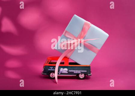 Kiew Ukraine - 11. März 2021. Spielzeugmodell von Volkswagen Typ 2, T1, Pickup 2 mit großer Geschenkbox auf dem Brett auf fett rosa Hintergrund mit Schatten. Stockfoto