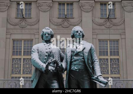 Weimar, Deutschland. 23rd Dez 2021. Das Goethe-Schiller-Denkmal am Theaterplatz ist schneebedeckt. Die bronzene Doppelstatue vor dem Deutschen Nationaltheater wurde im 19th. Jahrhundert vom Dresdner Bildhauer Ernst Rietschel entworfen. Quelle: Soeren Stache/dpa-Zentralbild/ZB/dpa/Alamy Live News Stockfoto