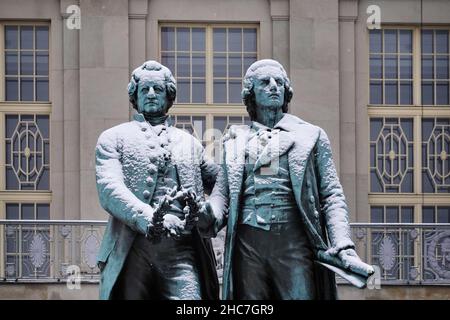 Weimar, Deutschland. 23rd Dez 2021. Das Goethe-Schiller-Denkmal am Theaterplatz ist schneebedeckt. Die bronzene Doppelstatue vor dem Deutschen Nationaltheater wurde im 19th. Jahrhundert vom Dresdner Bildhauer Ernst Rietschel entworfen. Quelle: Soeren Stache/dpa-Zentralbild/ZB/dpa/Alamy Live News Stockfoto