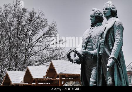 Weimar, Deutschland. 23rd Dez 2021. Das Goethe-Schiller-Denkmal am Theaterplatz ist schneebedeckt. Die bronzene Doppelstatue vor dem Deutschen Nationaltheater wurde im 19th. Jahrhundert vom Dresdner Bildhauer Ernst Rietschel entworfen. Quelle: Soeren Stache/dpa-Zentralbild/ZB/dpa/Alamy Live News Stockfoto