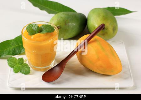 Mango Smoothie/Mango Lassi in einem Glas auf weißem Tisch mit Minzblättern und reifen und saftigen Mango Stockfoto