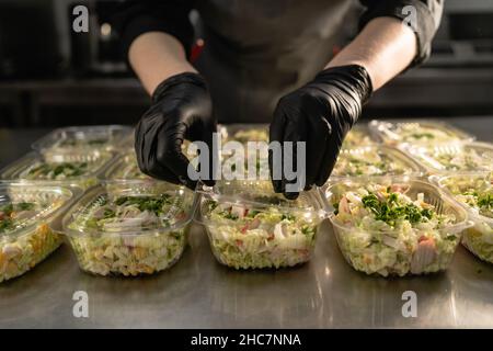 Gesunde Lieferung von Lebensmitteln. Gesunder Bio-Salat in einer Einwegschale. Sauberes Lebensmittelkonzept, gesundes Essen, Koch deckt Lunchboxen. Stockfoto