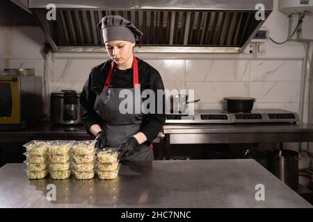 Die Köchin bereitet das Essen in einem Restaurant zu und bereitet es in Einweggerichten zu. Stockfoto