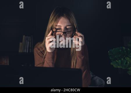 Müde junge Frau in Brille arbeitet nachts an einem Computer. Stockfoto