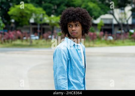 Serious afroamerikanischen männlichen jungen Erwachsenen mit afro haistyle im Sommer in der Stadt Stockfoto