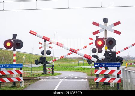 Bahnübergang mit sich schließenden Eisenbahnbäumen und blinkenden Warnleuchten. Der niederländische Text auf den Schildern besagt: Warten Sie, bis die rote Ampel aus ist, ein anderer Zug kann kommen. Stockfoto