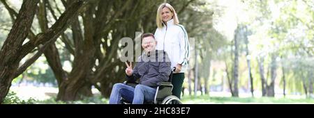 Frau, die im Park mit einem Mann im Rollstuhl läuft Stockfoto