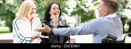 Mann im Rollstuhl, der mit Frauen im Park kommuniziert und lacht Stockfoto