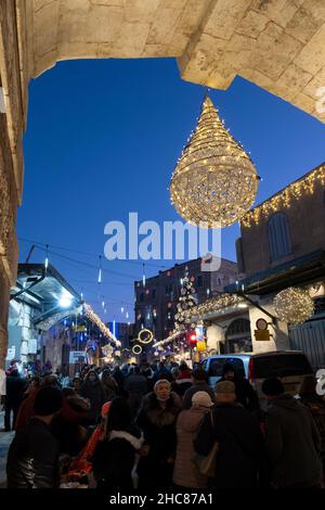 Jerusalem, Israel. 25th Dez 2021. Am 25. Dezember 2021 gehen die Menschen in Jerusalem, Israel, entlang einer weihnachtlich geschmückten Bab el Gadid Straße im christlichen Viertel der Altstadt. Israelis, die aufgrund der COVID-19-Omicron-Variante nicht ins Ausland reisen konnten, füllten die weihnachtlichen Gassen des Christlichen Viertels. Kredit: Eddie Gerald/Alamy Live Nachrichten Stockfoto