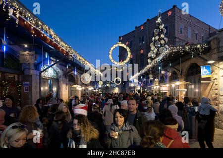 Jerusalem, Israel. 25th Dez 2021. Am 25. Dezember 2021 gehen die Menschen in Jerusalem, Israel, entlang einer weihnachtlich geschmückten Bab el Gadid Straße im christlichen Viertel der Altstadt. Israelis, die aufgrund der COVID-19-Omicron-Variante nicht ins Ausland reisen konnten, füllten die weihnachtlichen Gassen des Christlichen Viertels. Kredit: Eddie Gerald/Alamy Live Nachrichten Stockfoto