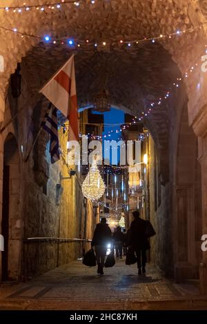 Jerusalem, Israel. 25th Dez 2021. Am 25. Dezember 2021 gehen die Menschen in Jerusalem, Israel, entlang einer weihnachtlich geschmückten Straße des griechischen Patriarchats im christlichen Viertel der Altstadt. Israelis, die aufgrund der COVID-19-Omicron-Variante nicht ins Ausland reisen konnten, füllten die weihnachtlichen Gassen des Christlichen Viertels. Kredit: Eddie Gerald/Alamy Live Nachrichten Stockfoto