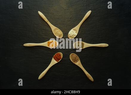 Fotografie von Pulvergewürzen in kleinen Holzlöffeln auf einem Schiefer als Hintergrund für Lebensmittel Stockfoto