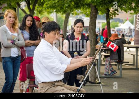 Toronto, Kanada - 1. Juli 2015: Kanadas Tag im Hafen von Toronto. Ein asiatischer männlicher Künstler malt ein Bild der Straße. Menschen beobachten mich Stockfoto