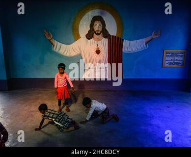 Haulia, Indien. 25th Dez 2021. Kinder kommen aus verschiedenen fernen Dörfern, um Heilige Weihnachten in einer kleinen und einzigen Kirche in der Gegend zu feiern und während der Bedrohung durch Omicron (Covid-19) in Indien in Haulia, Westbengalen, vor einem großen Jesus Christus-Foto ohne Maske zu spielen. (Foto von Soumyabrata Roy/Pacific Press/Sipa USA) Quelle: SIPA USA/Alamy Live News Stockfoto