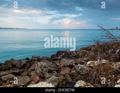 Eine Bucht mit kristallklarem Wasser mit Felsen im Vordergrund und einem bewölkten Himmel. Stockfoto