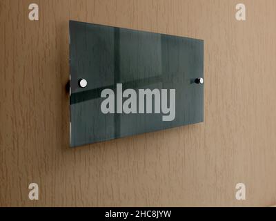 Dunkelgrünes breites rechteckiges Namensschild aus transparentem Glas auf Abstandhaltern aus Metall. Durchsichtiges Druckbrett für das Branding. Acryl dunkel Werbeschilder Stockfoto