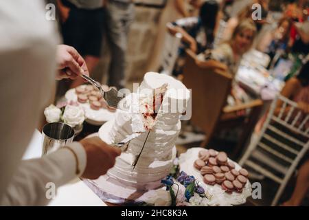 Die Hände des Mannes halten ein Stück Hochzeitstorte auf einem Messer und einem Spachtel Stockfoto